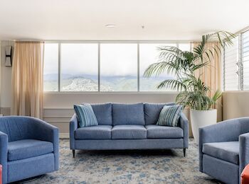 A bright living room with blue furniture, a large couch, armchairs, a potted plant, windows, and sheer curtains, finishing the sentence.