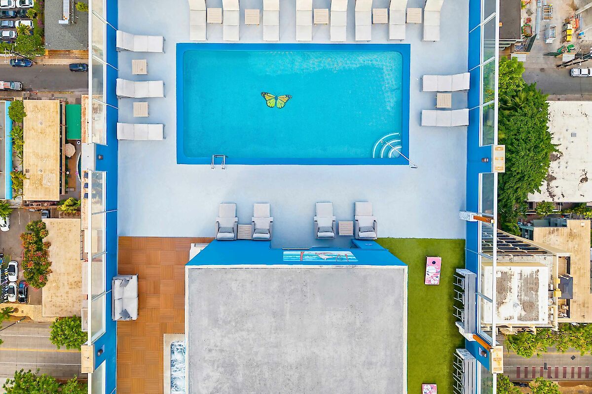 The image shows an aerial view of a rooftop pool area with loungers and a butterfly design in the pool's center.
