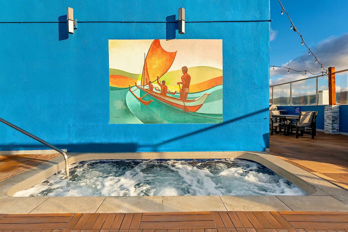 A jacuzzi with bubbling water is in front of a blue wall featuring a colorful mural of people in a boat.