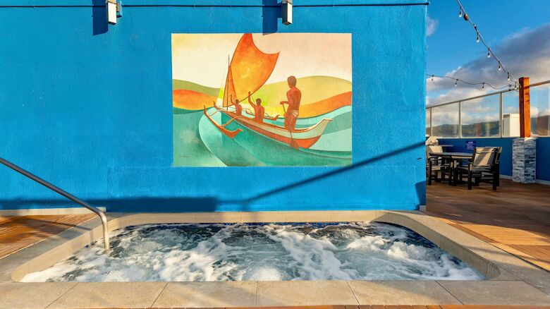 A jacuzzi with bubbling water is in front of a blue wall featuring a colorful mural of people in a boat.