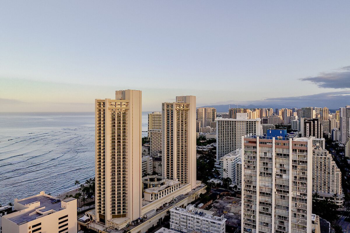 The image shows a coastal cityscape with tall buildings near the ocean under a clear sky during dusk or dawn, providing a serene view.