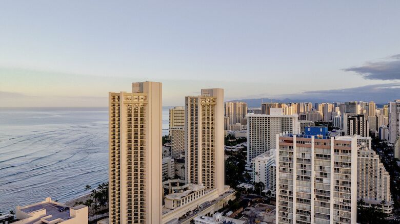 The image shows a coastal cityscape with tall buildings near the ocean under a clear sky during dusk or dawn, providing a serene view.