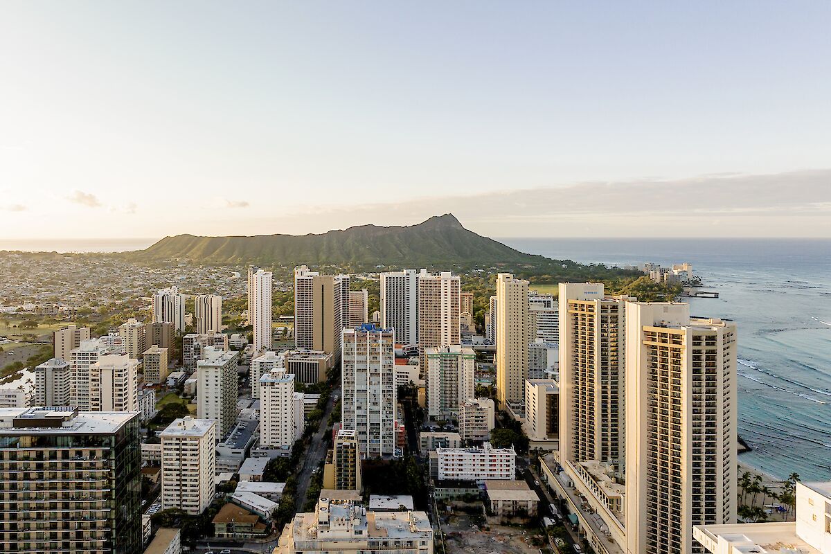 This image shows a cityscape with numerous high-rise buildings near a coastline, with a prominent mountain in the background and the ocean to the right.