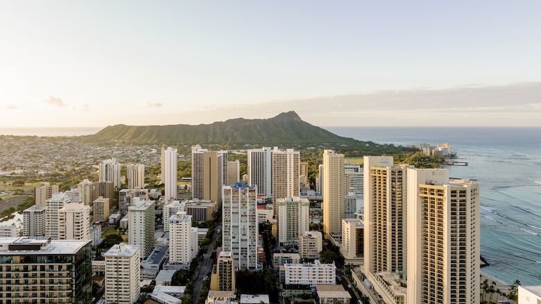 This image shows a cityscape with numerous high-rise buildings near a coastline, with a prominent mountain in the background and the ocean to the right.