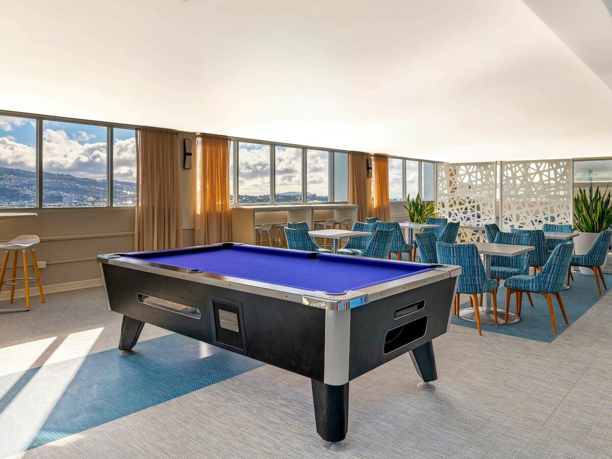A room with a pool table, lounge chairs, tables, and large windows offering a scenic view of mountains.