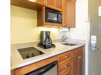 A compact kitchen features a microwave, coffee maker, stove, sink, and refrigerator with wooden cabinets and countertops, next to a door.